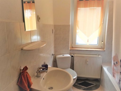 Kleines Badezimmer mit Dusche, Toilette und Waschbecken. Orangefarbene Vorhänge.